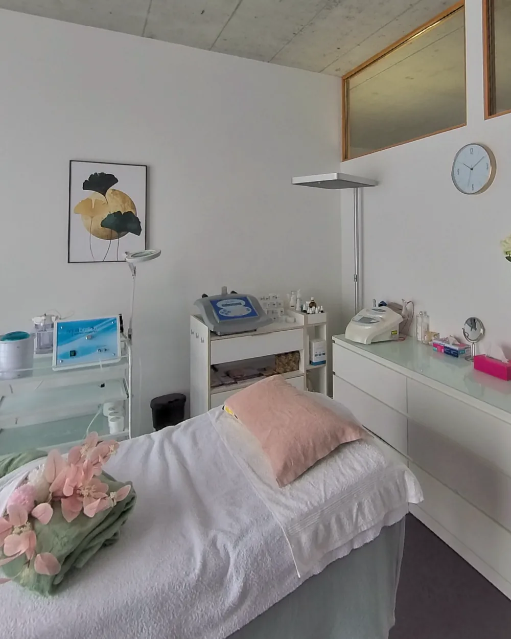 Behandlungsliege mit rosa Kissen und Orchideen, dahinter Geräte für Aquabrasion und Ultraschall