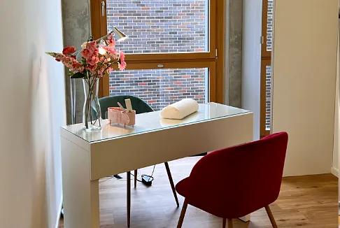 Maniküre-Tisch mit Blumen und rotem Stuhl am Fenster