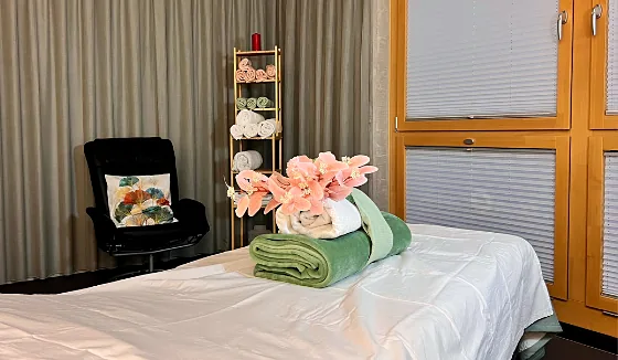 Massageliege mit Handtüchern und Orchidee, im Hintergrund ein Sessel